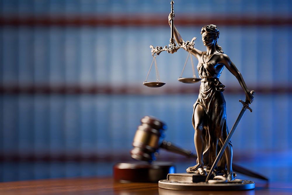 lady justice scale on top of a table with a gavel a blue bookshelf in the background